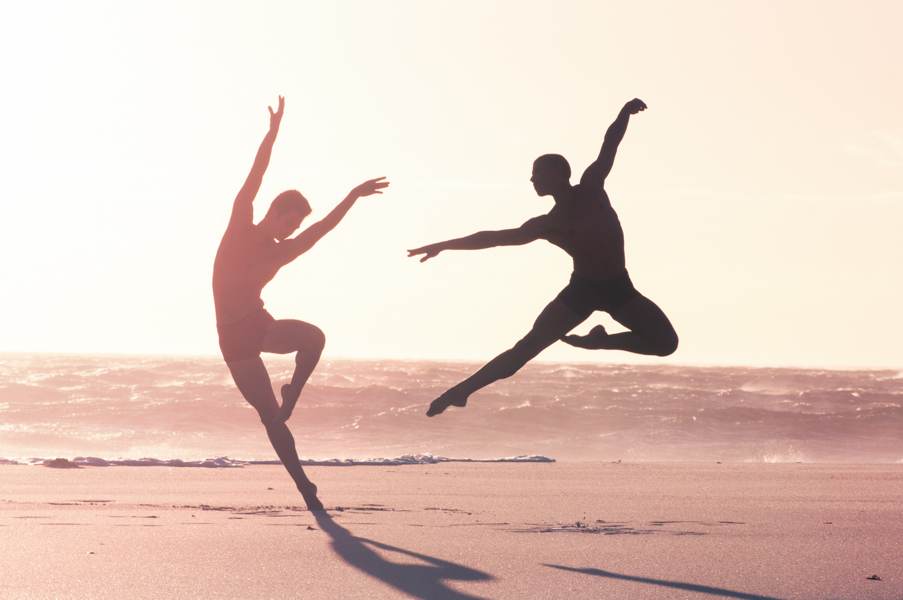 Two male dancers of the Cape Town City Ballet, doing jumps at sunset at Camps Bay Beach
